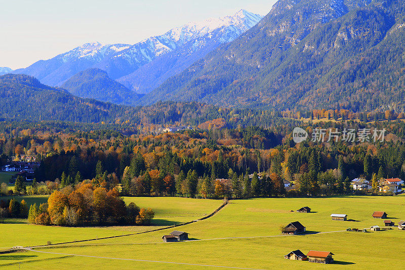 在谷仓农场和小木屋之上，阳光明媚的Garmisch Partenkirchen阿尔卑斯村庄在巴伐利亚阿尔卑斯山从Alpspitze，田园诗般的松树林地秋季景观，雄伟的阿尔卑斯山谷，戏剧性的巴伐利亚德国雪山全景，德国